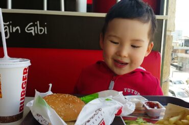 Sweet baby boy eating hamburger with ketchup, fries and juice in Burger King fast food restaurant.