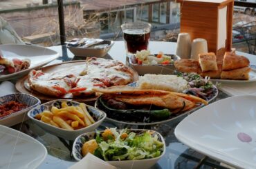 Female hand taking hot pizza on served dining table. Appetizing pizza, french fries, salad and