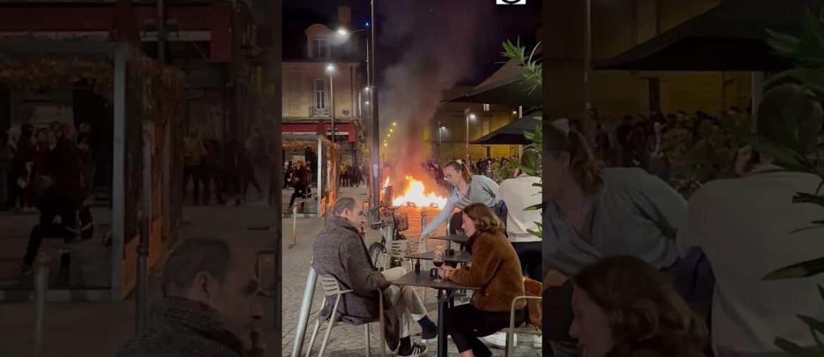 Diners enjoy wine amid the glow of a fire lit by demonstrators in France
