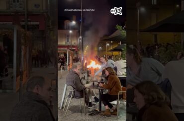 Diners enjoy wine amid the glow of a fire lit by demonstrators in France