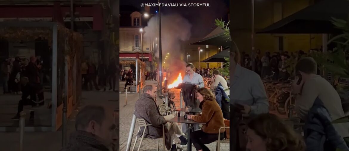 Diners sit outside a cafe in Bordeaux, France enjoying wine amid a raging fire lit by demonstrators