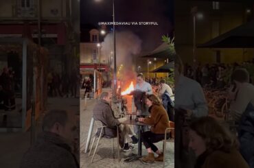 Diners sit outside a cafe in Bordeaux, France enjoying wine amid a raging fire lit by demonstrators