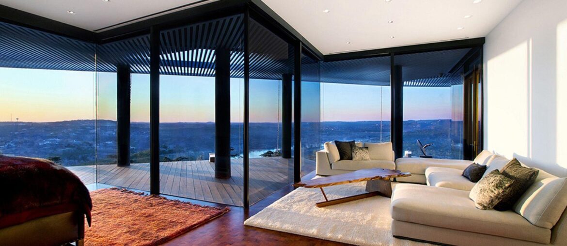 Bedroom features angled, floor-to-ceiling glass walls providing a view of Lake Austin in Austin, Texas. [1800 × 1197]