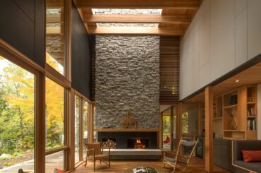 Tall wood living room with a fireplace clad with locally sourced granite in a woodland retreat located along the shores of Contau Lake, Haliburton County, Ontario, Canada [2364×2432]