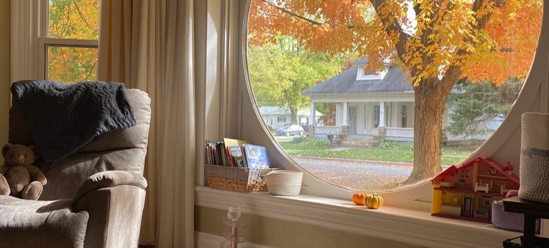 Room with autumn views through a round window in a renovated Midwest Victorian home [1124x1406]