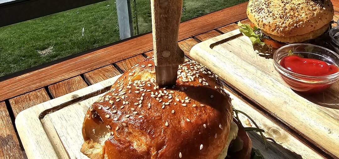 Beef Burger (minced beef, cheese, tomatoes, gherkins, melted onions, rocket) with a side salad; and a Vegan Burger (with a cauliflower patty, lettuce, tomato, cucumber, sprouts and chive cream) with fries; served at the lake near Radolfzell, Germany