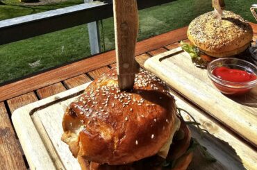 Beef Burger (minced beef, cheese, tomatoes, gherkins, melted onions, rocket) with a side salad; and a Vegan Burger (with a cauliflower patty, lettuce, tomato, cucumber, sprouts and chive cream) with fries; served at the lake near Radolfzell, Germany