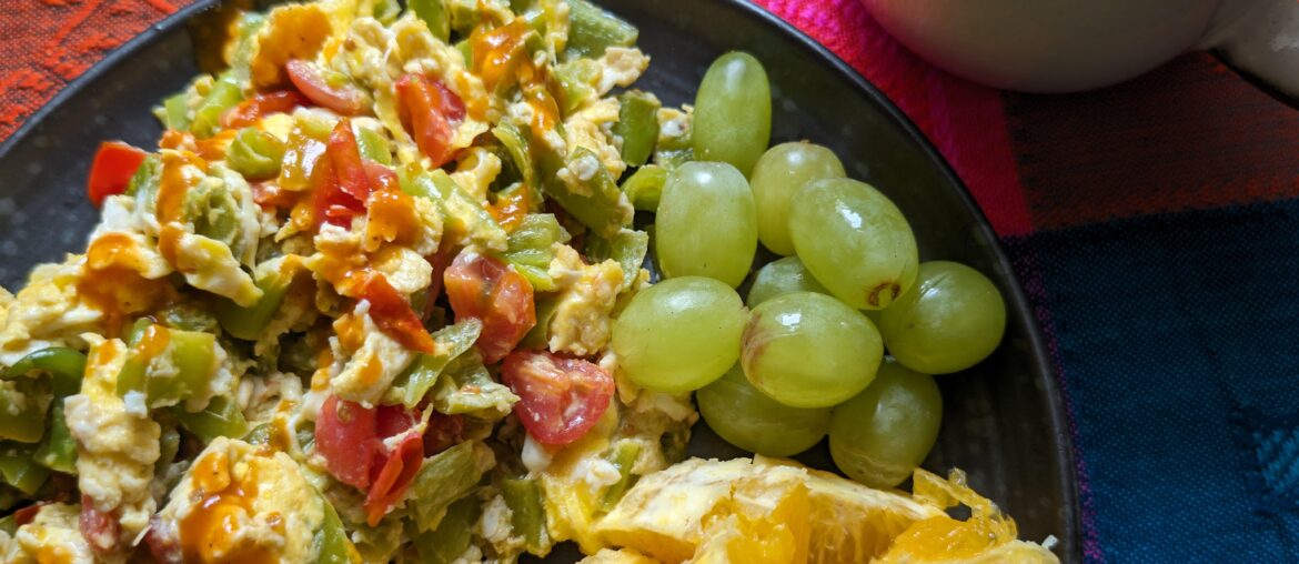 Scrambled eggs with green peppers, tomato. Grapes and orange. Café au lait.