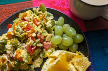 Scrambled eggs with green peppers, tomato. Grapes and orange. Café au lait.