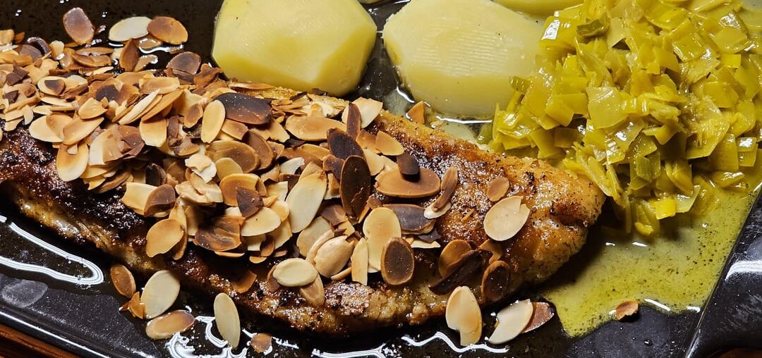 Fried fillet of pike-perch with roasted almonds in a lemon-butter sauce, with leek in a curry-white wine sauce, boiled potatoes and red radish sprouts