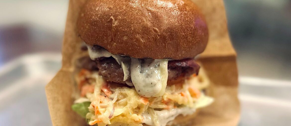 Burger with brioche bun, beef patty, lettuce, bacon, coleslaw salad, truffle mayo and cheddar cheese